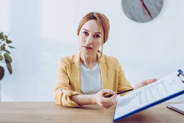 Attractive recruiter in yellow jacket holding clipboard and pen — Stock Photo