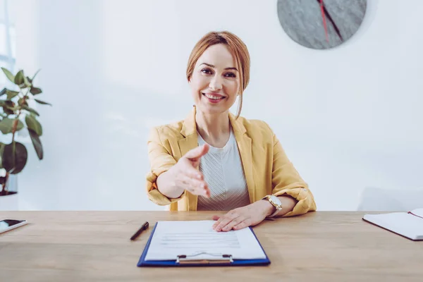 Happy recruiter in yellow jacket gesturing while sitting near clipboard and pen — Stock Photo