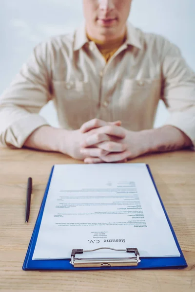 Selective focus of clipboard with resume cv lettering near pen and man with clenched hands — Stock Photo