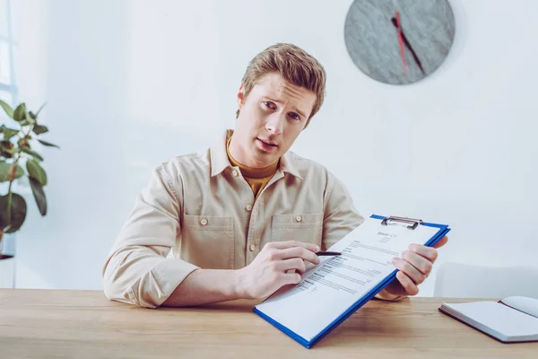 Schöner Personalvermittler zeigt mit Stift auf Klemmbrett, während er in die Kamera schaut — Stockfoto