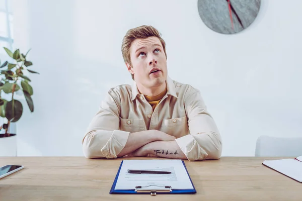 Bored handsome recruiter sitting near clipboard and pen in office — Stock Photo