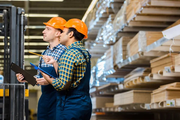 Zwei multikulturelle Arbeiter in Uniform lächeln und Klemmbretter in der Hand halten — Stockfoto