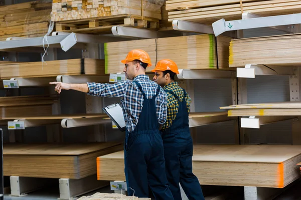 Magazzino lavoratore punta con il dito mentre in piedi vicino amico indiano — Foto stock