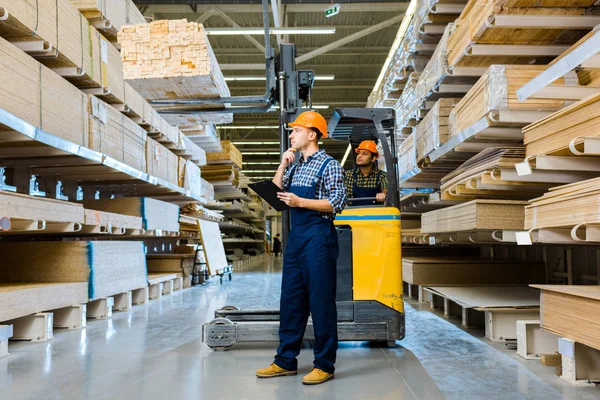 Indiano magazzino lavoratore seduto in carrello elevatore vicino premuroso collega con appunti — Foto stock