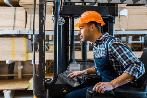 Concentrated handsome worker in uniform and helmet operating forklift machine — Stock Photo