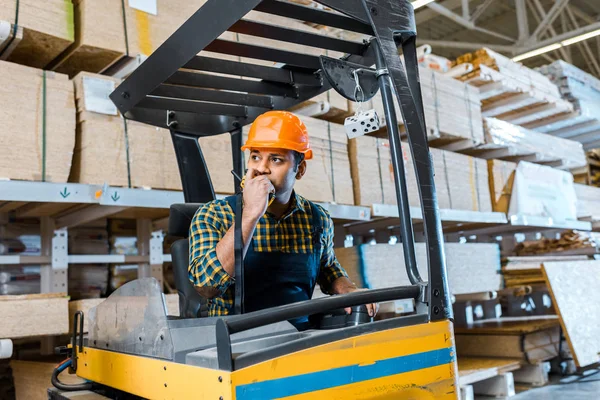 Indian warehouse worker talking on walkie talkie while sitting in forklift machine — Stock Photo