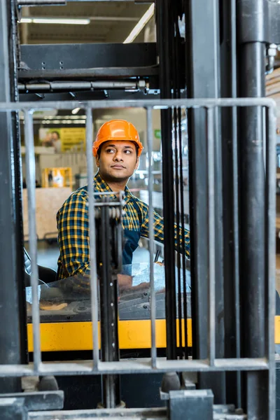 Bonito, trabalhador indiano atencioso sentado na máquina de empilhadeira no armazém — Fotografia de Stock