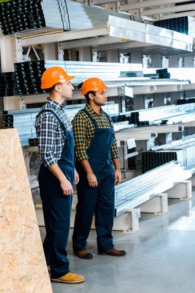 Dos amigos multiculturales serios en uniforme de pie en el almacén - foto de stock