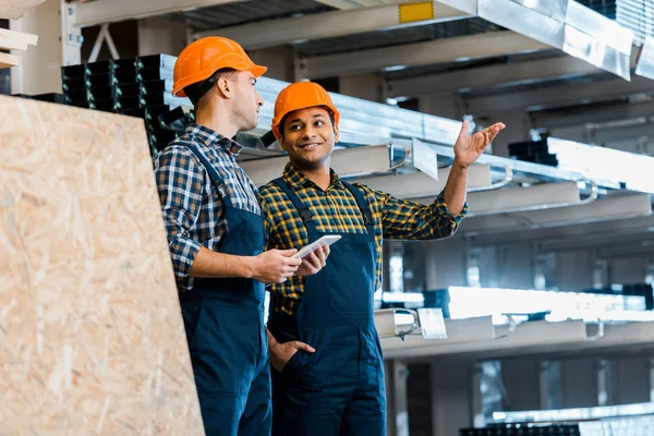 Lavoratore magazzino indiano sorridente che punta con mano vicino bel collega — Foto stock