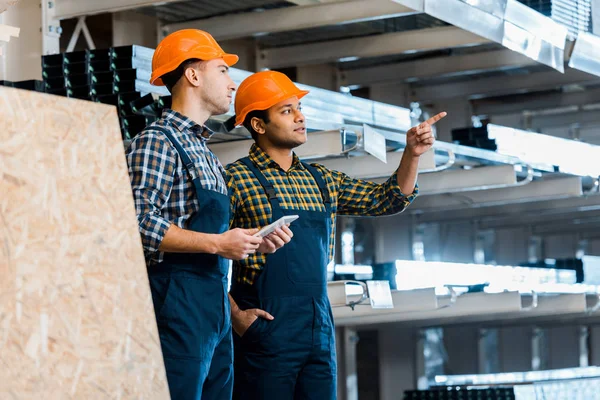 Attentive indian warehouse worker pointing with hand near handsome colleague — Stock Photo