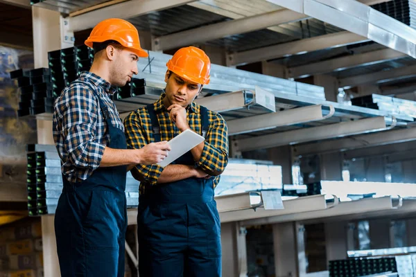 Trabajadores de almacenes multiculturales reflexivos en uniforme usando tableta digital - foto de stock