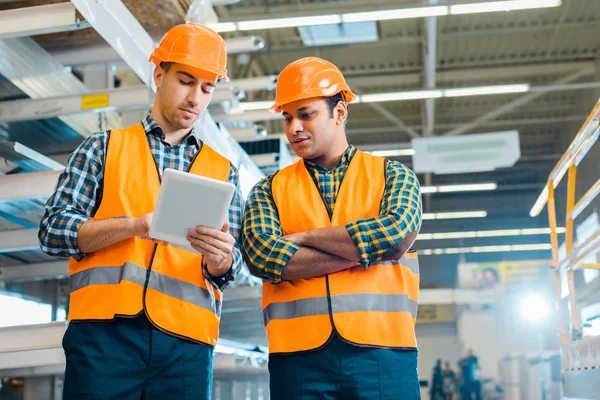 Trabajadores multiculturales y concentrados que utilizan tabletas digitales en el almacén - foto de stock