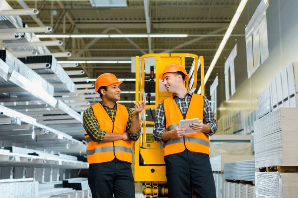 Selective focus of cheerful multicultural workers talking while standing near scissor lift — Stock Photo