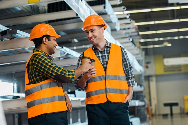 Selective focus of multicultural workers clinking with paper cups in warehouse — Stock Photo