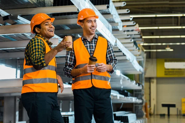 Laughing multicultural workers holding paper cups and looking away in warehouse — Stock Photo