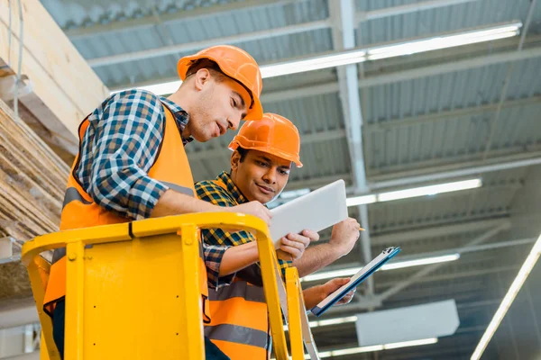 Concentrated multicultural workers using digital tablet while standing on scissor lift — Stock Photo