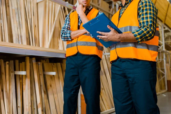 Partial view of workers standing near shelves with wooden construction materials — Stock Photo