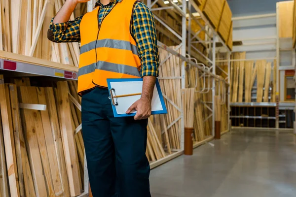 Partial view of warehouse worker in safety vast holding clipboard — Stock Photo