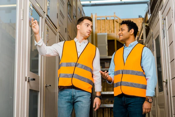 Multicultural warehouse workers talking while standing in doors department — Stock Photo