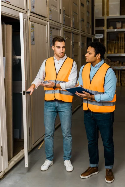 Trabajador de almacén guapo abriendo la puerta cerca de colega indio - foto de stock