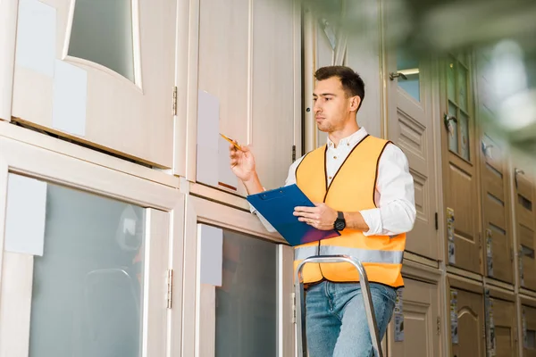 Selective focus of worker in safety vest standing on ladder in warehouse — Stock Photo