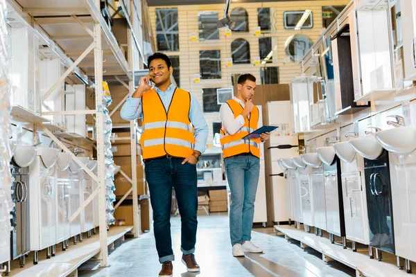 Smiling indian worker talking on smartphone near colleague with clipboard in plumbing department — Stock Photo