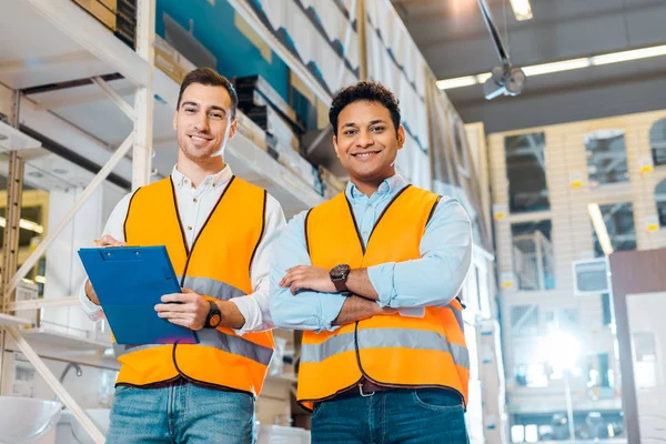 Sonrientes trabajadores de almacenes multiculturales sonriendo y mirando a la cámara - foto de stock