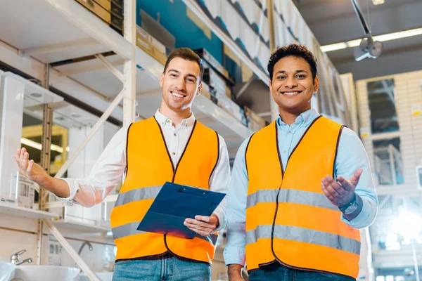Smiling multicultural warehouse workers in safety vests smiling and looking at camera — Stock Photo