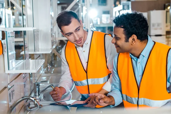Smiling multicultural colleagues in safety vests working in plumbing department — Stock Photo