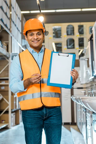 Lächelnder indischer Arbeiter zeigt mit leerem Papier auf Klemmbrett und blickt in die Kamera — Stockfoto