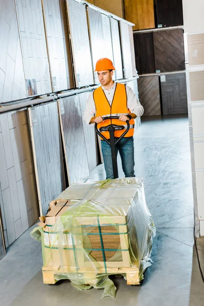 Bello, serio lavoratore che trasporta pallet jack con materiali da costruzione — Foto stock