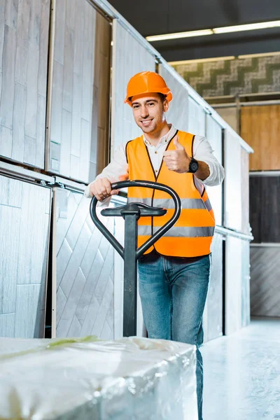 Trabalhador sorrindo carregando palete jack e mostrando polegar para cima — Fotografia de Stock