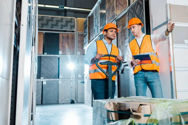 Magazziniere che punta con mano vicino collega indiano con presa pallet — Foto stock