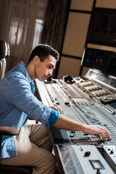 Apuesto productor de sonido de raza mixta trabajando en la consola de mezcla en el estudio de grabación - foto de stock