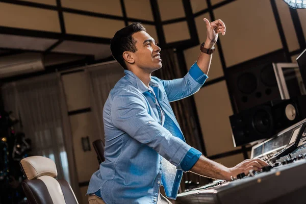 Lächelnder Mixed Race Soundproduzent gestikuliert während er im Tonstudio arbeitet — Stockfoto