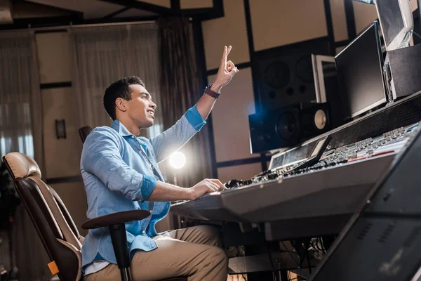 Красивый продюсер смешанного расового звука показывает знак победы во время работы в студии звукозаписи — стоковое фото
