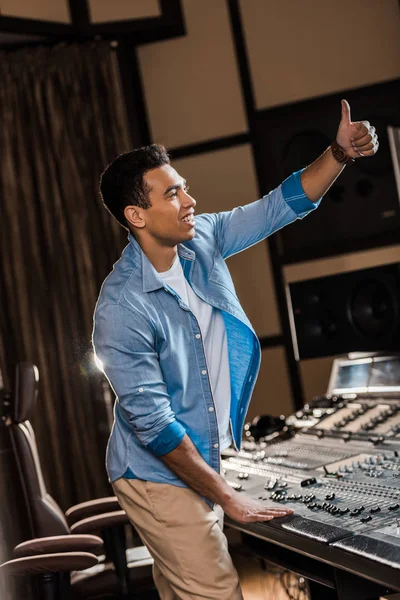 Smiling mixed race sound producer showing thumb up while working at mixing console — Stock Photo