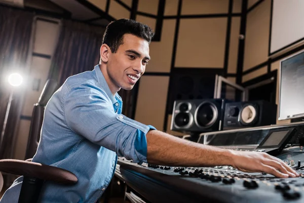 Smiling mixed race sound producer working at mixing console in recording studio — Stock Photo