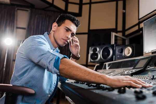 Apuesto, productor de sonido de raza mixta atento trabajando en la consola de mezcla - foto de stock