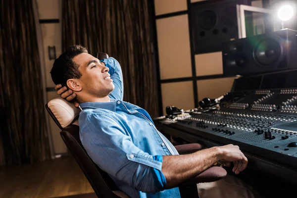 Producteur sonore mixte souriant relaxant dans une chaise de bureau dans un studio d'enregistrement — Photo de stock