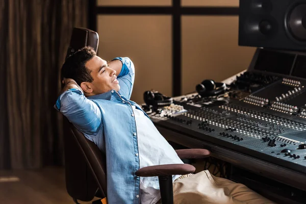 Bonito sorrindo misturado raça som produtor descansando no escritório cadeira no estúdio de gravação — Fotografia de Stock