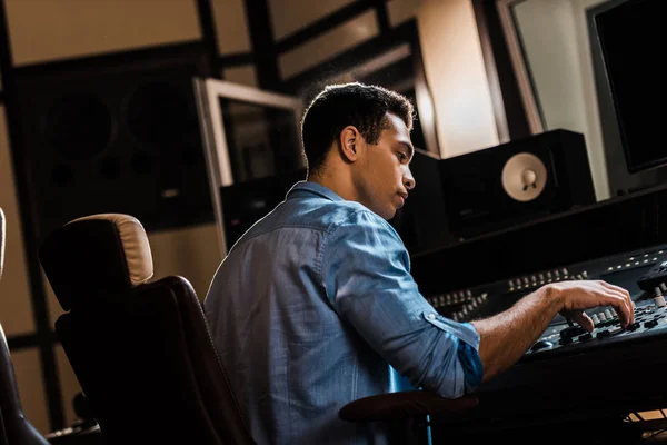 Serious mixed race sound producer working at mixing console in recording studio — Stock Photo