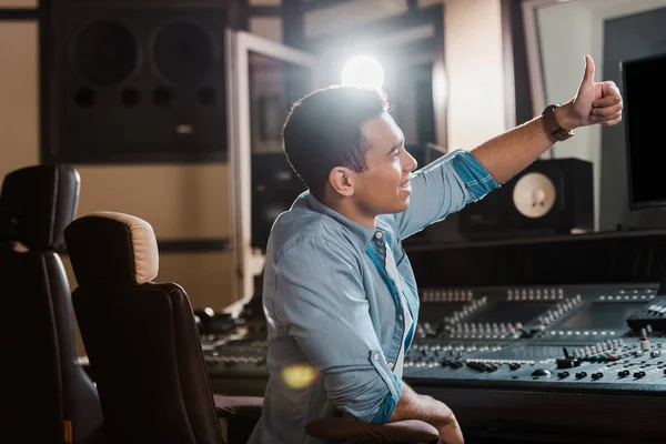 Producteur sonore mixte souriant montrant pouce levé tout en travaillant dans un studio d'enregistrement — Photo de stock