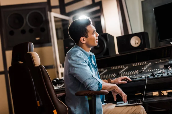 Красивый улыбающийся продюсер смешанного расового звука, работающий в студии звукозаписи на микширующей консоли — стоковое фото