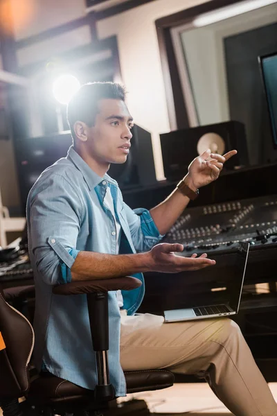 Serious mixed race sound producer gesturing while sitting at  mixing console in recording studio — Stock Photo