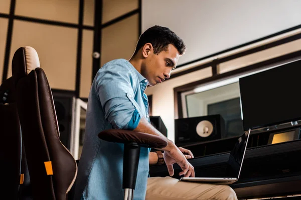 Serio produttore di suoni di razza mista che utilizza laptop in studio di registrazione — Foto stock