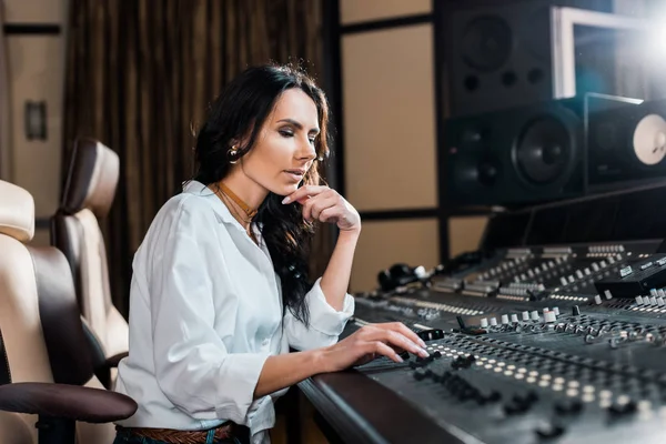 Belo produtor de som concentrado trabalhando no console de mixagem em estúdio de gravação — Fotografia de Stock