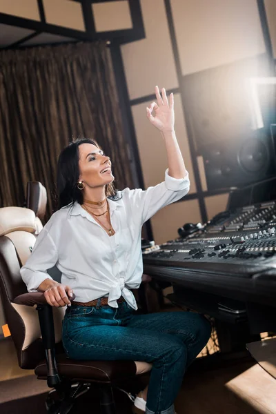 Attractive sound producer showing ok sign and smiling in recording studio — Stock Photo