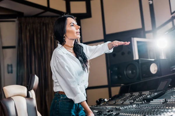 Beautiful sound producer gesturing while working at mixing console in recording studio — Stock Photo