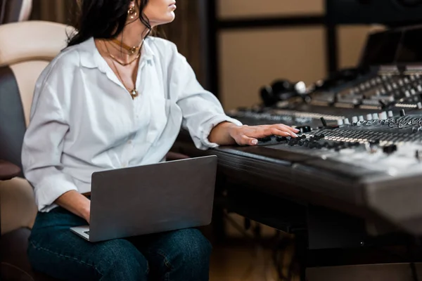 Vista recortada del productor de sonido que trabaja en la consola de mezcla y el uso de ordenador portátil - foto de stock